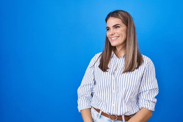 西班牙裔年轻女子站在蓝色的背景上 面带微笑 表情自然地望向一旁 充满自信地大笑 — 图库照片