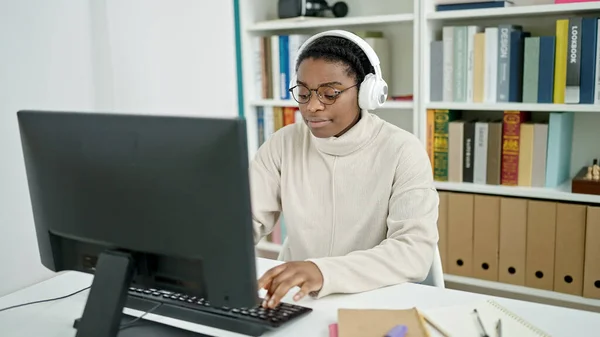 アフリカ系アメリカ人の女性が図書館大学でコンピューターとヘッドフォンを使って学ぶ — ストック写真