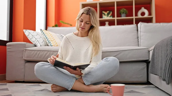 年轻的金发女人坐在家里看书 喝咖啡 — 图库照片
