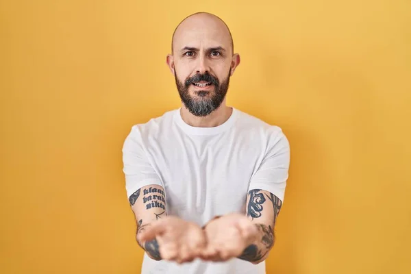Mladý Hispánec Tetováním Stojící Nad Žlutým Pozadím Usmívající Dlaněmi Přijímá — Stock fotografie
