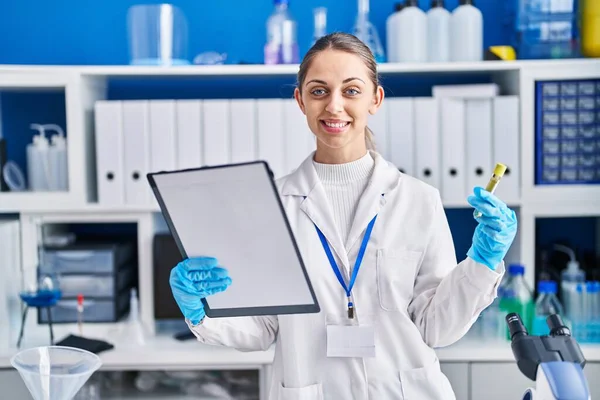 年轻女科学家微笑着 自信地在实验室拿着试管阅读文件 — 图库照片