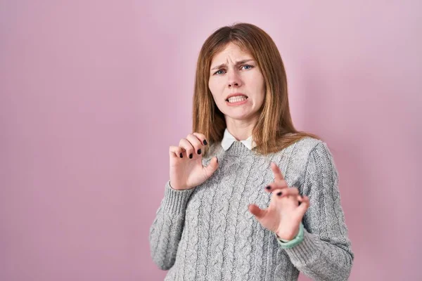 Beautiful woman standing over pink background disgusted expression, displeased and fearful doing disgust face because aversion reaction.