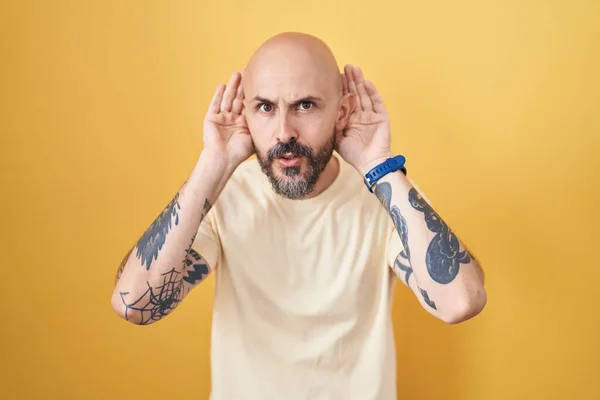 Homem Hispânico Com Tatuagens Sobre Fundo Amarelo Tentando Ouvir Ambas — Fotografia de Stock