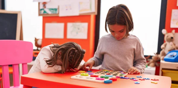 可爱的男孩和女孩坐在幼儿园的桌子上玩数学拼图游戏 — 图库照片