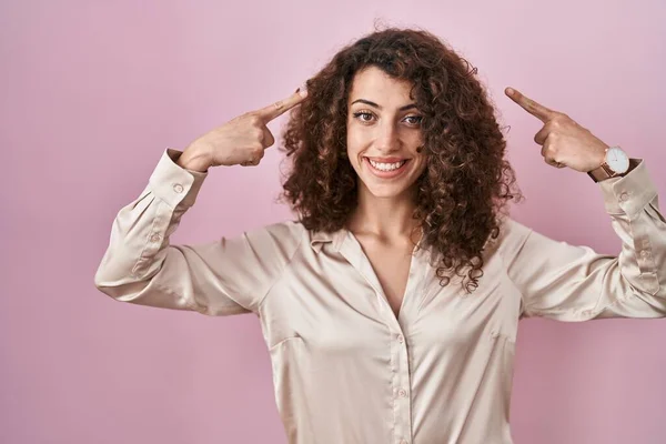 Hispanic Woman Curly Hair Standing Pink Background Smiling Pointing Head — Zdjęcie stockowe
