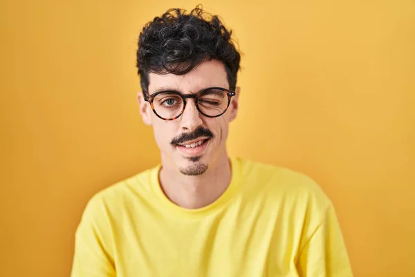 Hombre Hispano Con Gafas Pie Sobre Fondo Amarillo Guiñando Ojo — Foto de Stock