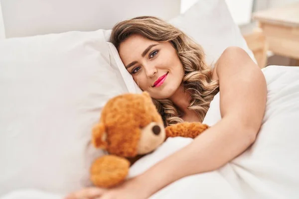 Mujer Joven Sonriendo Confiada Acostada Cama Con Oso Peluche Dormitorio — Foto de Stock