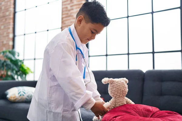 Roztomilý Hispánský Chlapec Nosí Lékařskou Uniformu Zkoumá Medvídka Doma — Stock fotografie