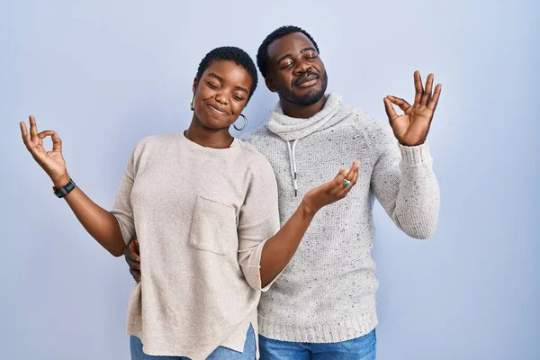 站在蓝色背景上的年轻的非洲裔美国夫妇一起放松了下来 闭眼微笑着 用手指做冥想动作 瑜伽概念 — 图库照片