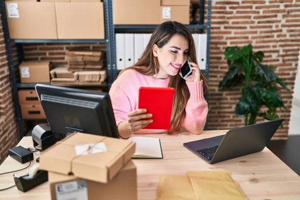 stock image Young beautiful hispanic woman ecommerce business worker using touchpad talking on smartphone at office