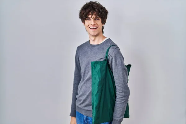 再利用可能なバッグを身に着けている若い男はポジティブで幸せな立っていると笑顔で自信を持って笑顔を見せて歯 — ストック写真