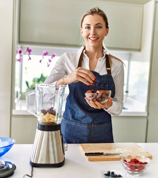 Young blonde woman smiling confident pouring dates on blender at kitchen