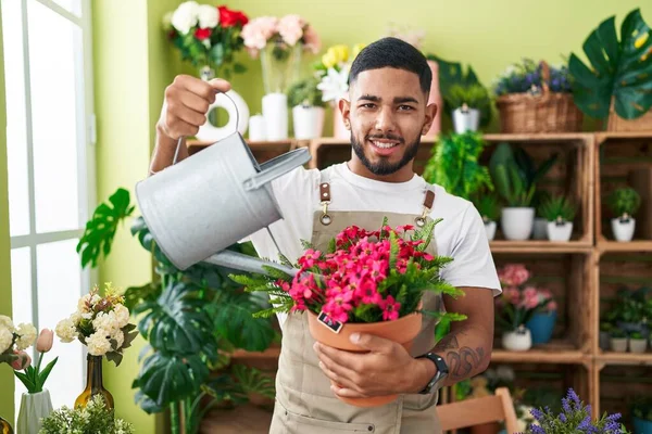 Young latin man florist watering plant at flower shop