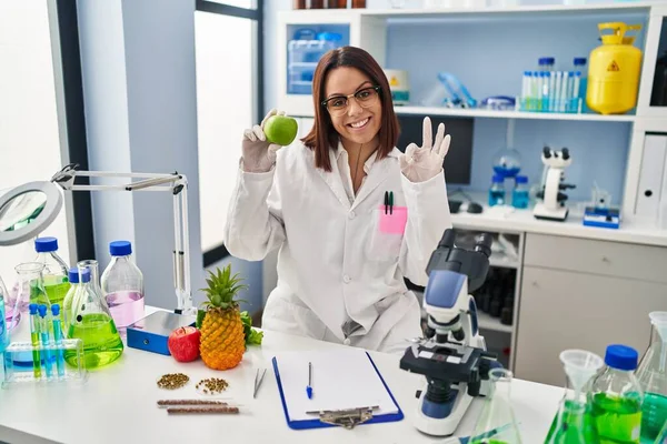 Mulher Hispânica Jovem Trabalhando Laboratório Cientista Segurando Frutas Fazendo Sinal — Fotografia de Stock