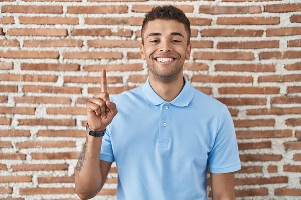自信と幸せを笑顔ながら レンガの壁の上に立っているブラジルの若者は 指の数1を示すと指摘します — ストック写真