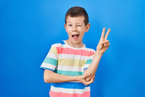青い背景の上に立っている若い白人の子供は カメラで勝利のサインを指で行う幸せな顔をして笑っています — ストック写真