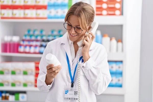 Młoda Blondynka Dziewczyna Farmaceuta Trzymając Tabletki Butelki Rozmowy Telefonicznej Aptece — Zdjęcie stockowe