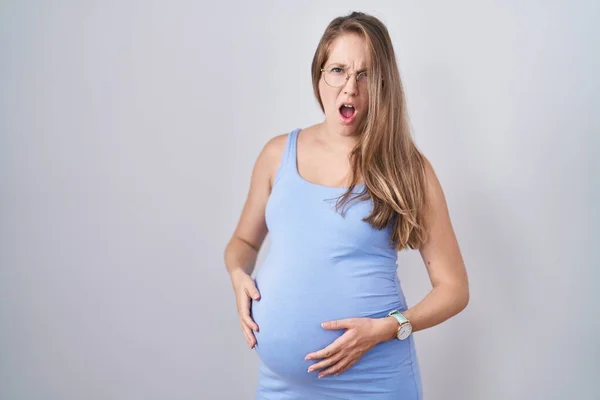若いです妊娠中の女性はショック顔で白い背景の上に立って 懐疑的で皮肉を探して オープン口で驚いて — ストック写真