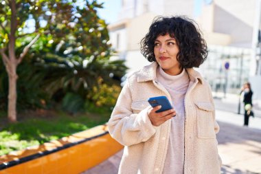 Parkta akıllı telefon kullanarak gülümseyen güzel bir İspanyol kadın.