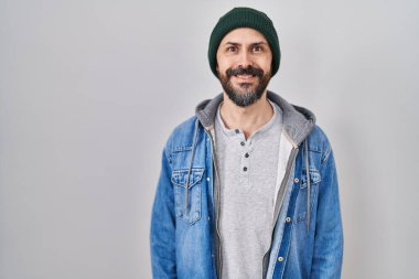 Yüzünde mutlu ve havalı bir gülümseme olan yün şapkalı İspanyol dövmeli genç bir adam. şanslı kişi. 