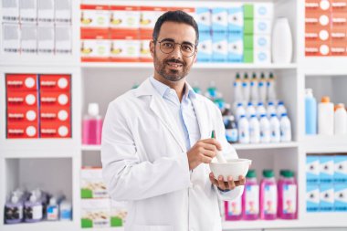 Young hispanic man pharmacist smiling confident working at pharmacy