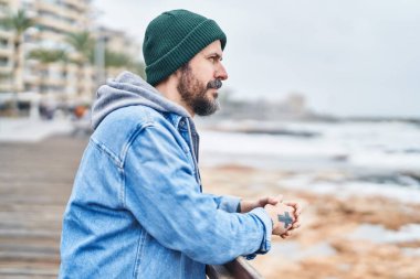 Genç kel bir adam, deniz kenarında ciddi bir ifadeyle Balustrade 'a yaslanıyor.