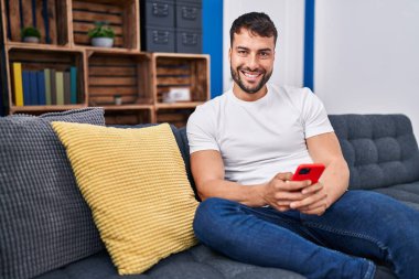 Evdeki kanepede oturan, akıllı telefon kullanan genç bir İspanyol.