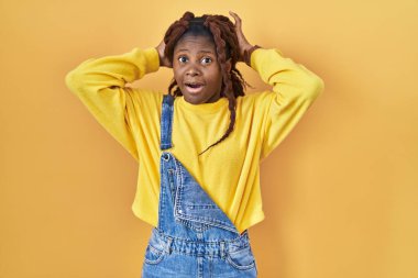 Sarı arka planda dikilen Afrikalı kadın deli ve elleri başının üstünde korkmuş ve ağzı açık şok geçirmekten korkmuş. 