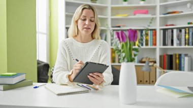 Genç sarışın kız öğrenci kütüphane üniversitesinde dokunmatik bir yere çiçek saksısı çiziyor.