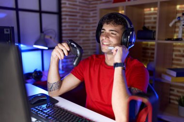 Young hispanic man streamer playing video game using joystick at gaming room
