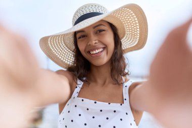 Young african american woman wearing summer hat make selfie by camera at seaside