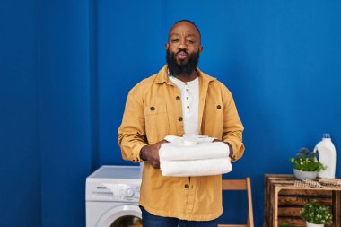 Çamaşır odasında temiz havlu tutan Afro-Amerikalı bir adam öpüşürken kameraya bakıyor. Sevimli ve seksi. aşk ifadesi. 