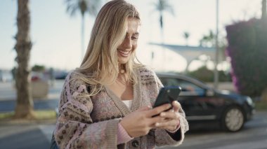Sokakta akıllı telefon kullanan, kendine güvenen genç sarışın kadın.