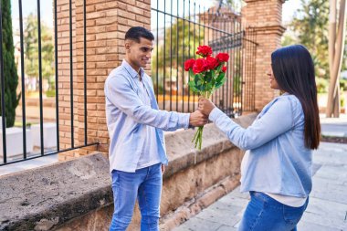 Young latin couple expecting baby surprise with flowers at street