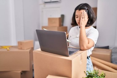 Young woman using laptop with worried expression at new home
