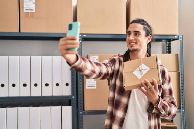 Genç adam ecommerce iş çalışanı paket tutuyor. Ofisteki akıllı telefondan selfie çekiyor.