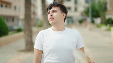Non binary man using handfan suffering for hot at park