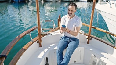 Limanda teknede oturan orta yaşlı bir adam akıllı telefon kullanıyor.