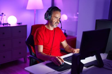 Middle age man streamer playing video game using computer at gaming room