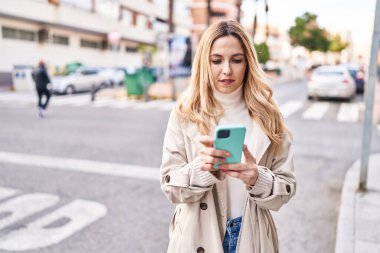 Sokakta akıllı telefon kullanan genç sarışın kadın.