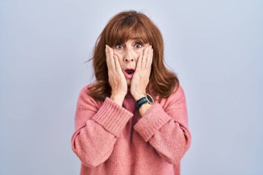 Orta yaşlı İspanyol bir kadın izole edilmiş arka planda duruyor. Korkmuş ve şok olmuş, şaşırmış ve şaşırmış bir halde. 