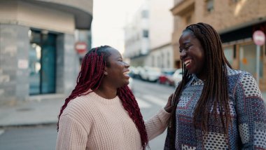 İki Afro-Amerikalı arkadaş gülerek sokakta bir arada duruyorlar.