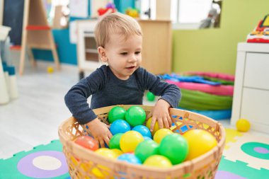 Anaokulunda yerde taşaklarıyla oynayan sevimli sarışın çocuk.