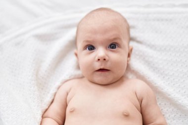 Adorable caucasian baby lying on bed with relaxed expression at bedroom