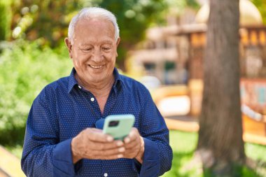 Senior grey-haired man smiling confident using smartphone at park