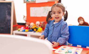 Adorable hispanic girl smiling confident sitting on floor at kindergarten