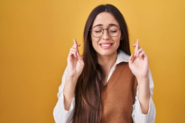 Sarı arka planda duran genç esmer kadın gözlüklü işaret parmağı takmış umut ve gözler kapalı gülümseyerek. Şans ve batıl inançlar. 