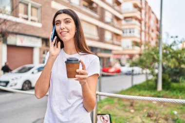 Young beautiful hispanic woman talking on smartphone drinking coffee at street