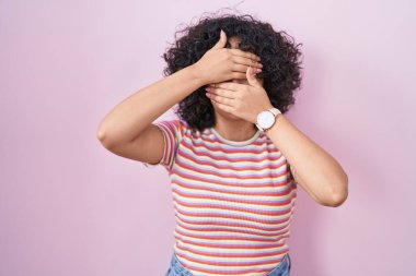 Pembe arka planda duran genç ortadoğulu kadın gözlerini ve ağzını ellerle kapatıyor, şaşırmış ve şok olmuş. duygu gizleme 