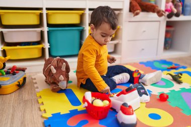 Anaokulunda yerde oturmuş süpermarket oyunu oynayan sevimli İspanyol çocuk.